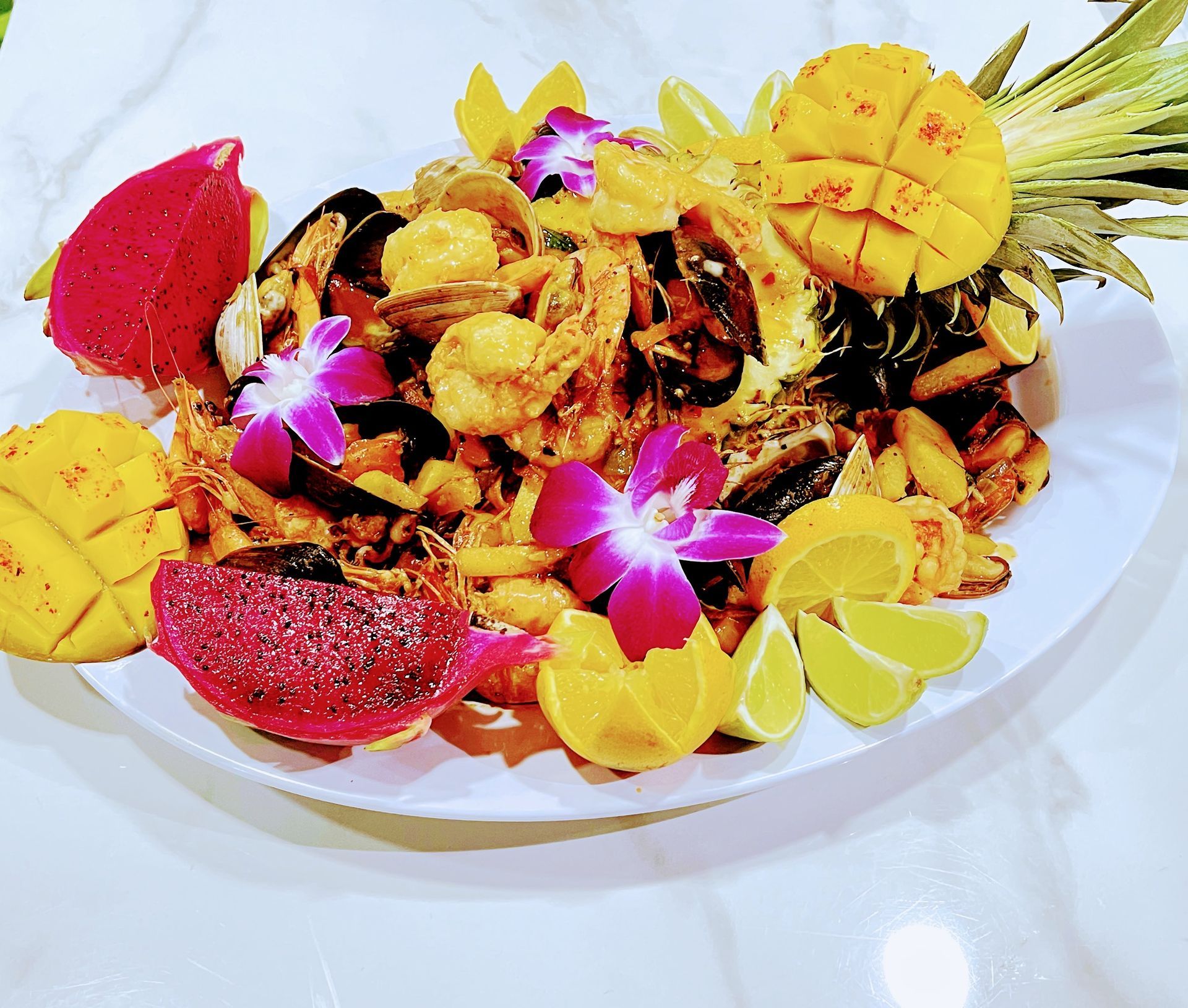 Seafood boil in a pineapple bowl, garnished with dragon fruit, mango, and orchids.