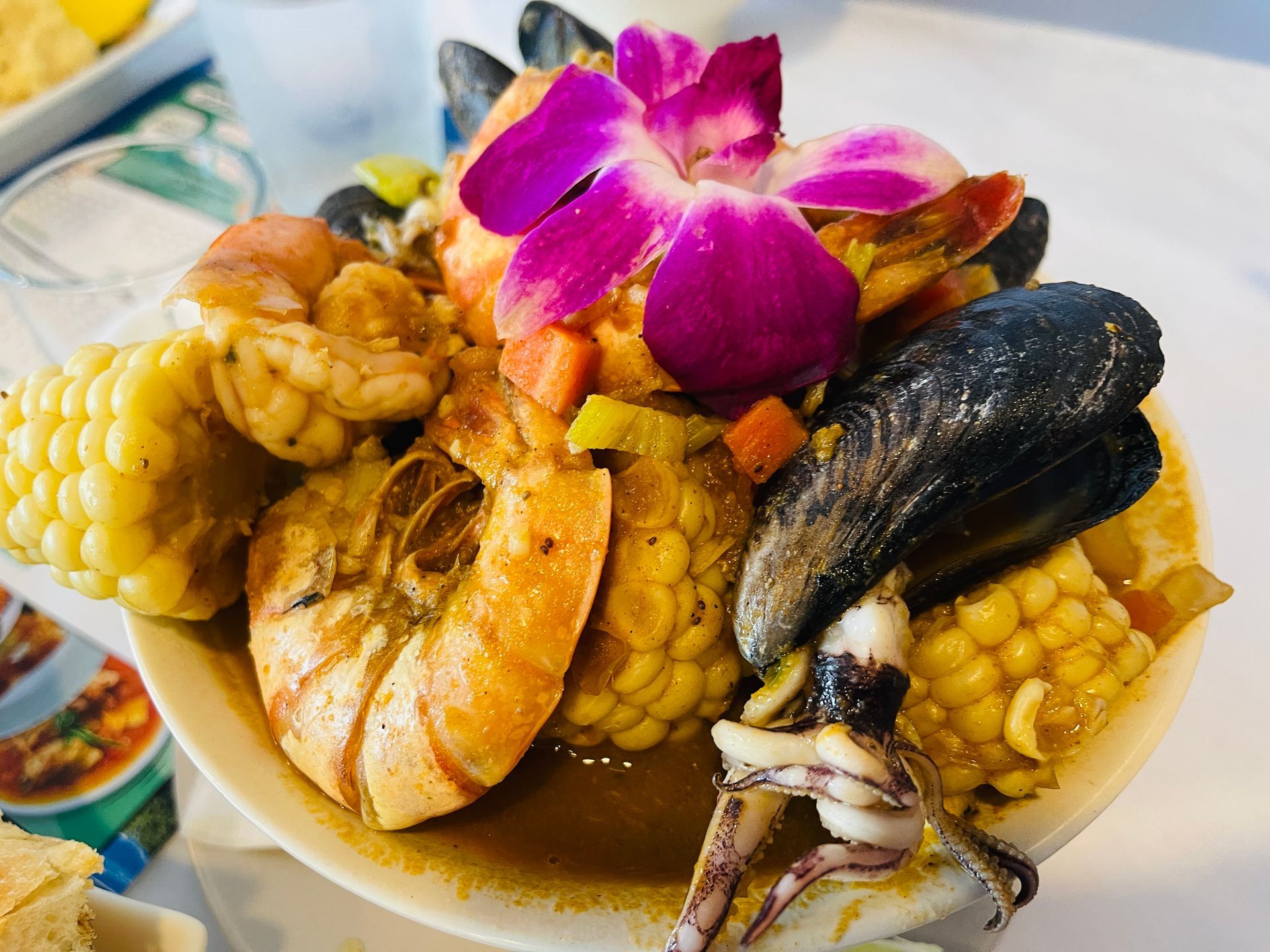Seafood boil with shrimp, mussels, corn, and an orchid in a white bowl.