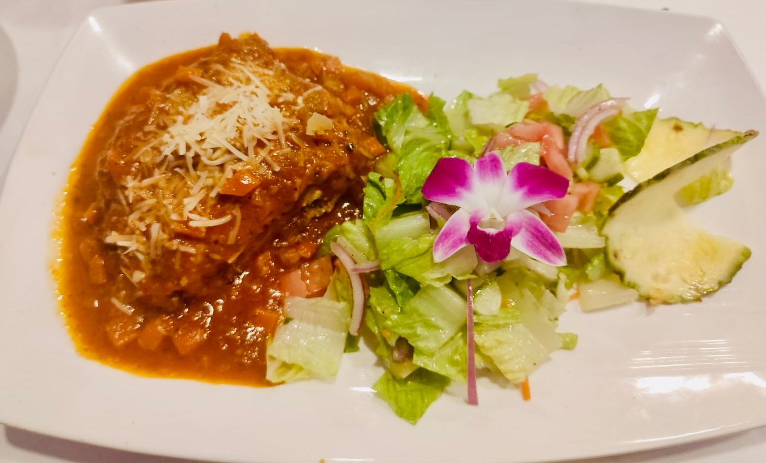 Meatloaf with red sauce, garnished with cheese, served with salad and pineapple on a white plate.