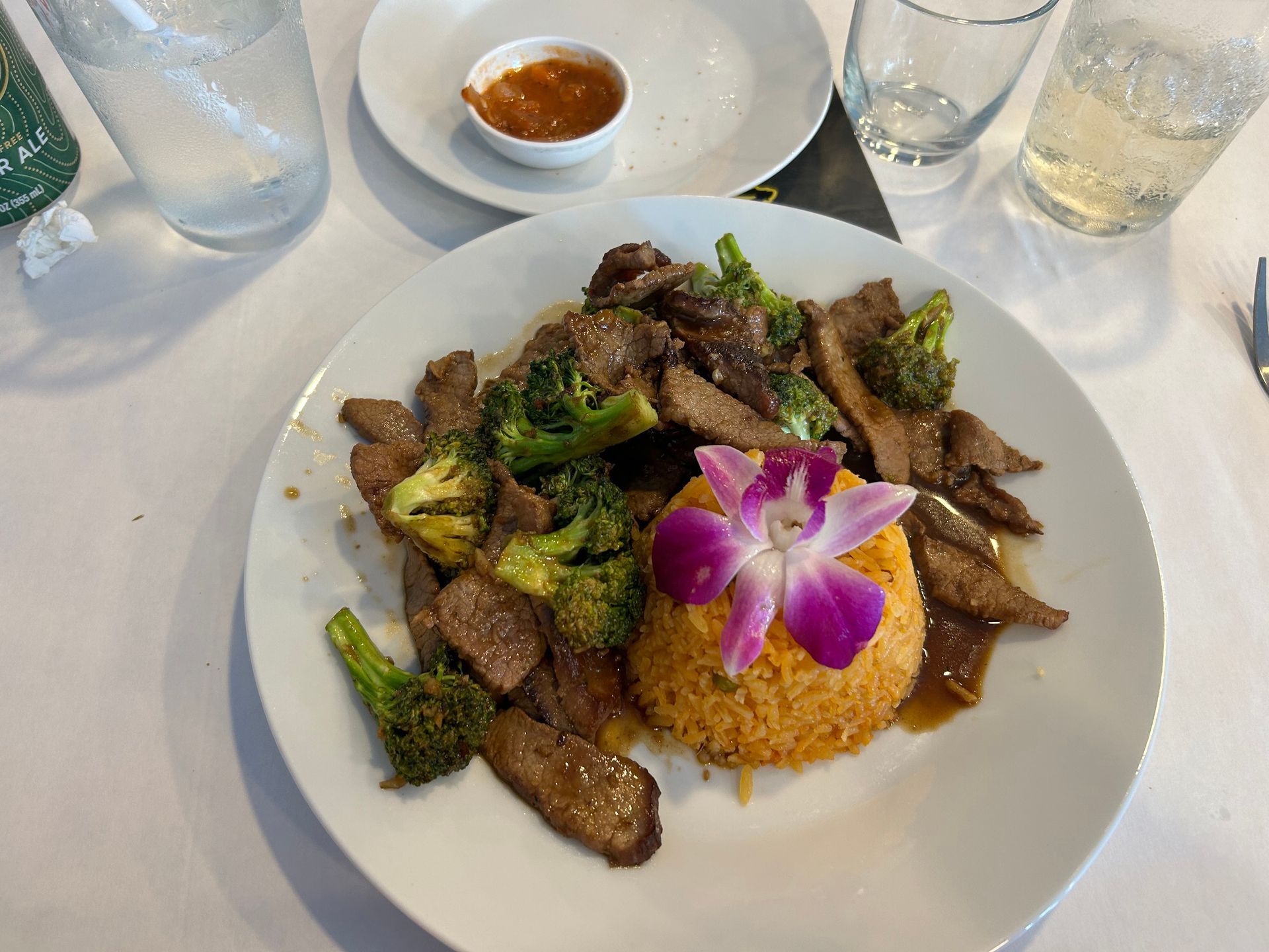 Beef and broccoli dish with rice and flower garnish on a white plate.