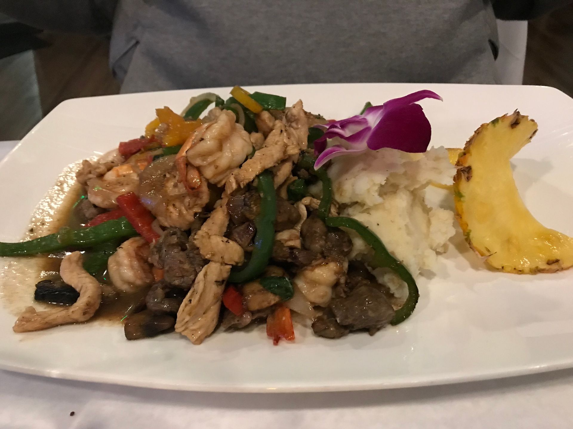 Chicken and vegetables with pineapple on a white plate, garnished with a purple orchid.
