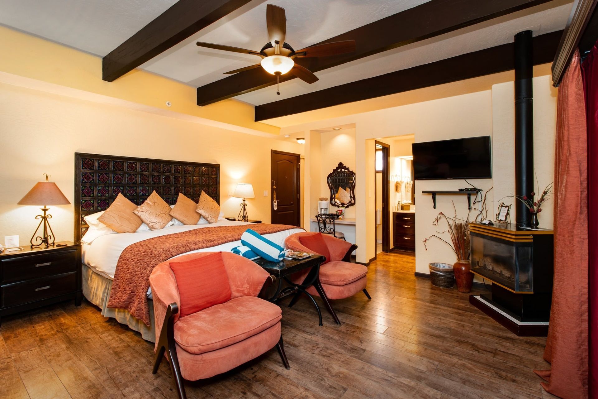 A bedroom with a king size bed , two chairs , a television and a fireplace.