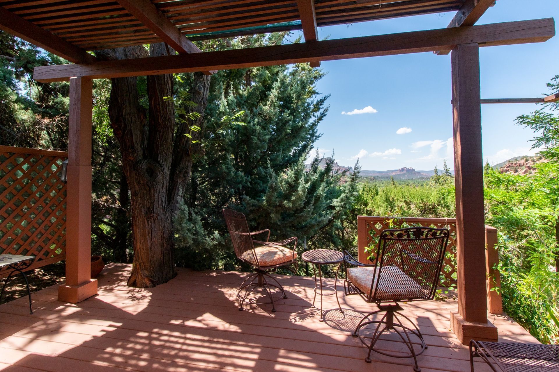 A wooden deck with a table and chairs under a pergola.