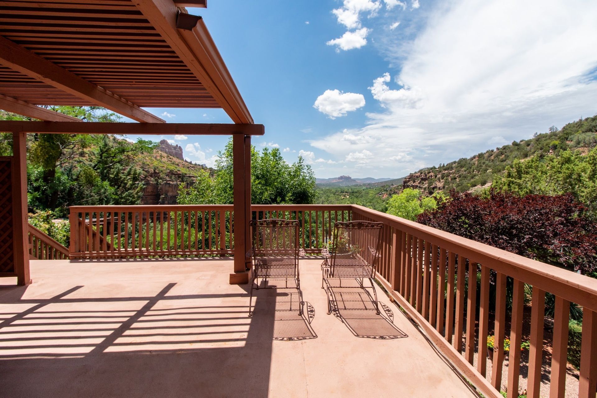 A wooden deck with chairs and a pergola overlooking a mountain.