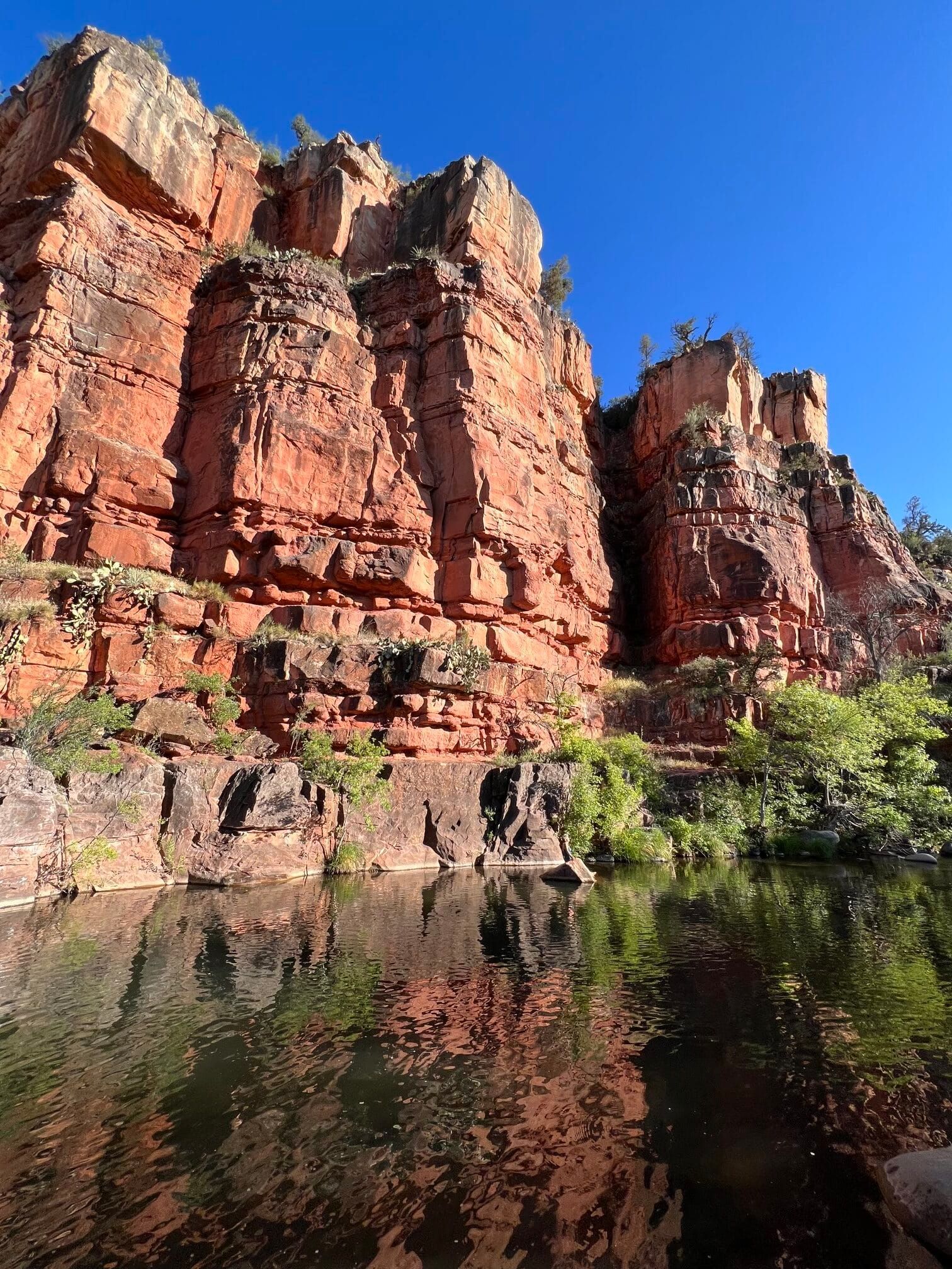 A large rocky cliff is reflected in a body of water.