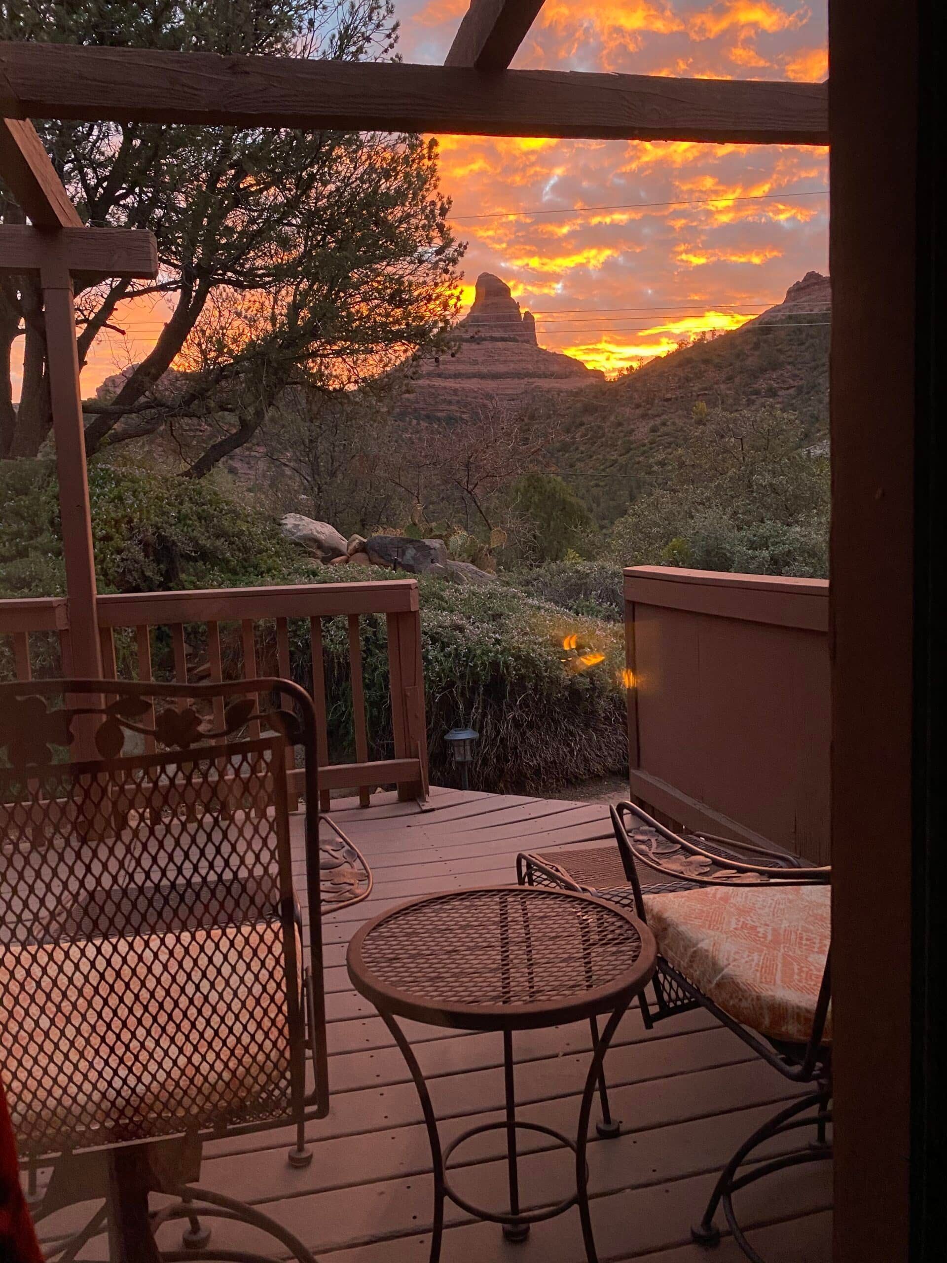 A view of a sunset from a deck with a table and chairs.