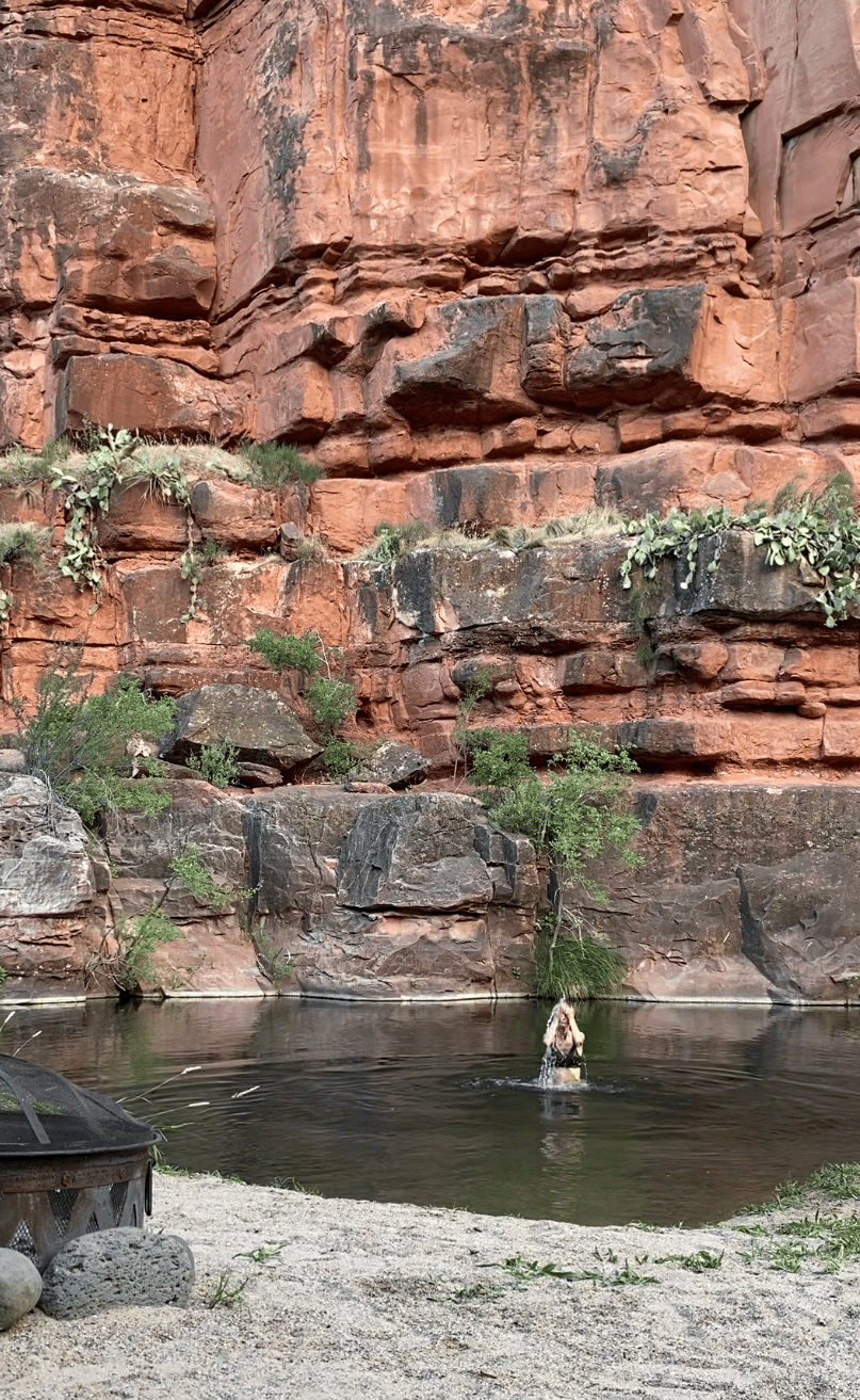 A person is swimming in a river next to a rock wall.