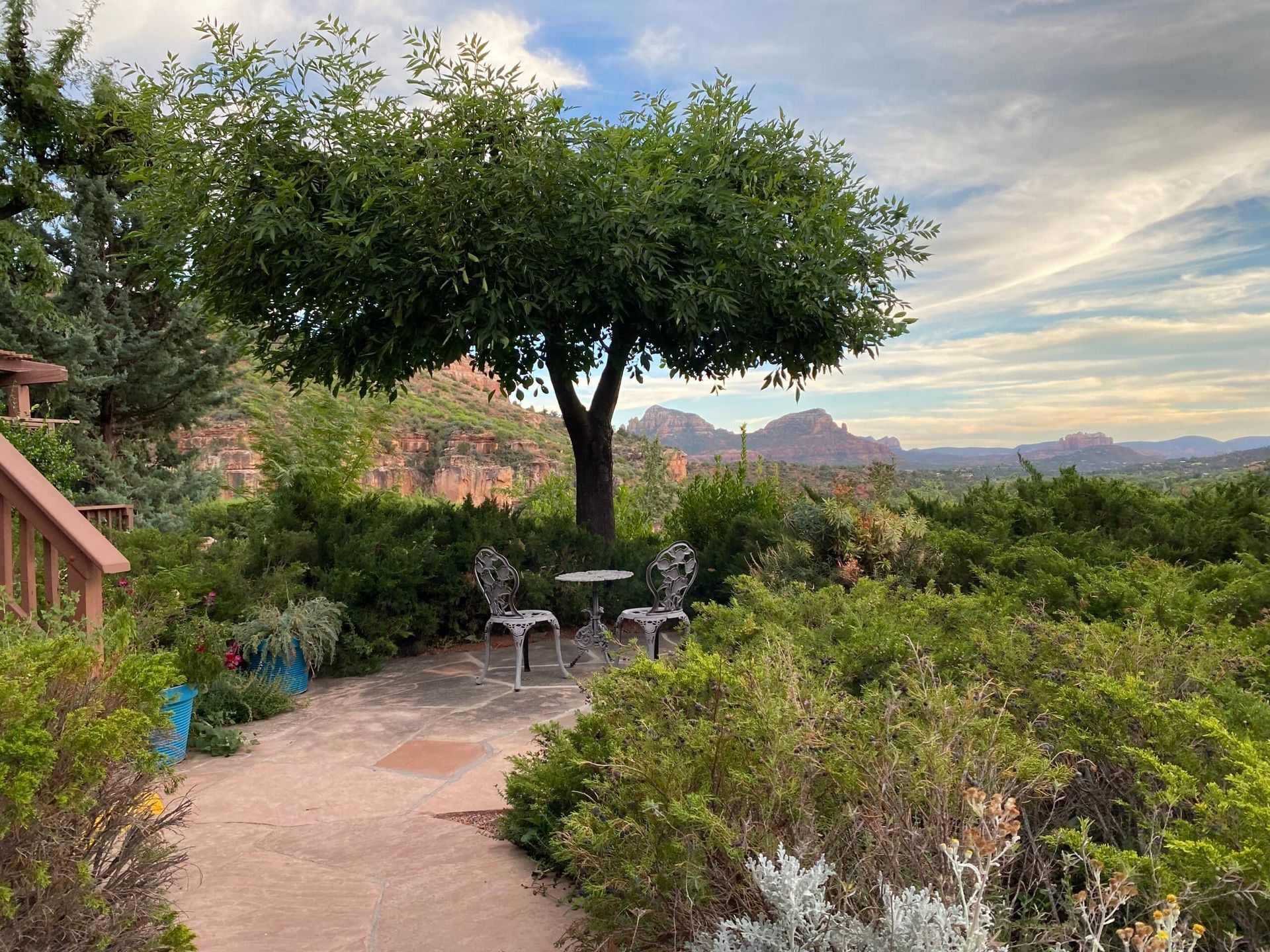 A patio with a table and chairs under a tree with mountains in the background.