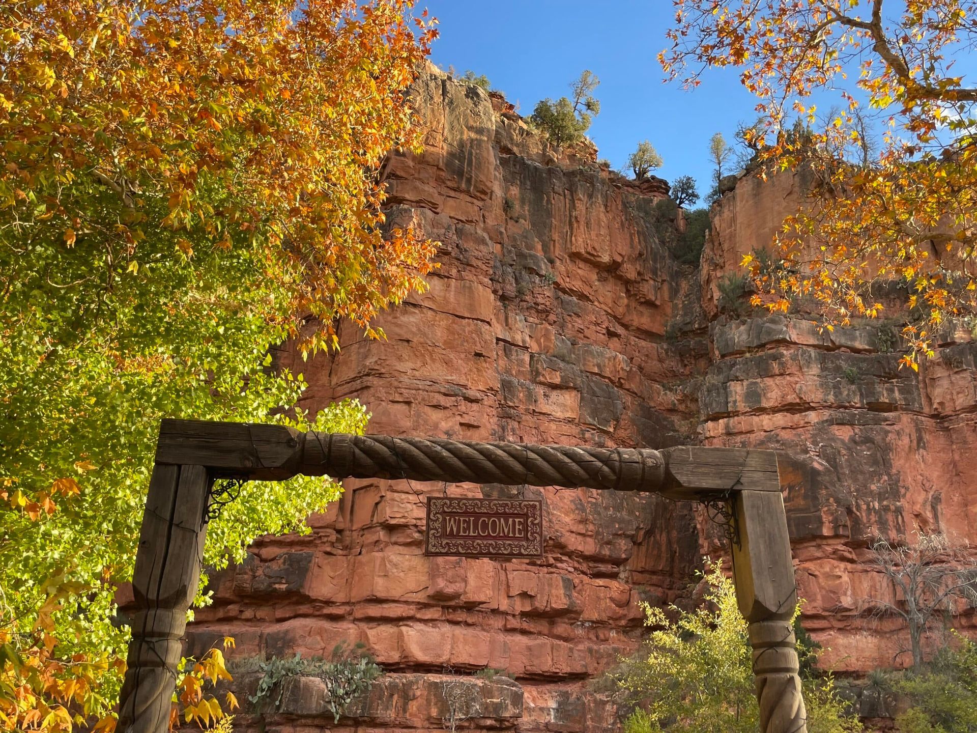 A wooden archway in front of a cliff with trees in the foreground.