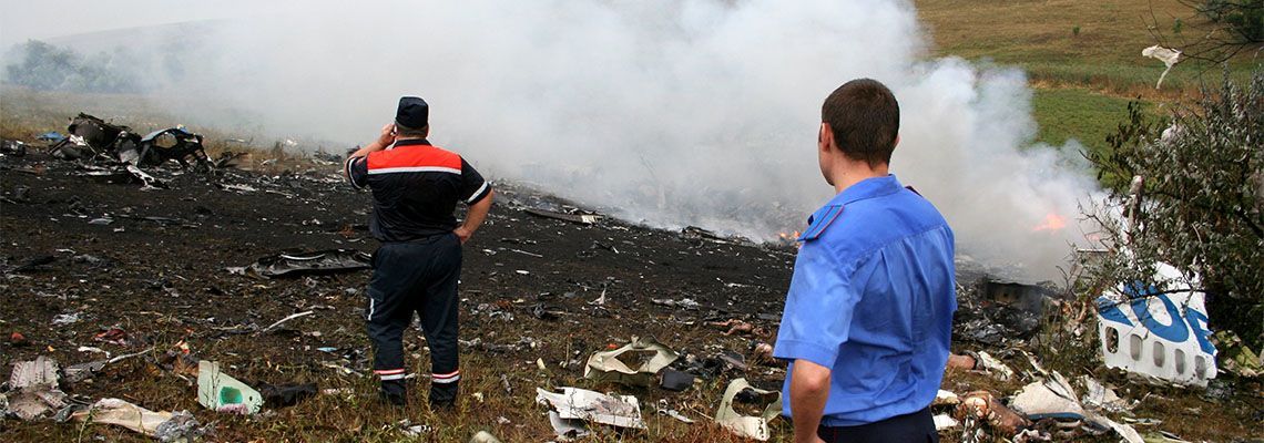 Two people standing near a smoky trash fire in a littered field