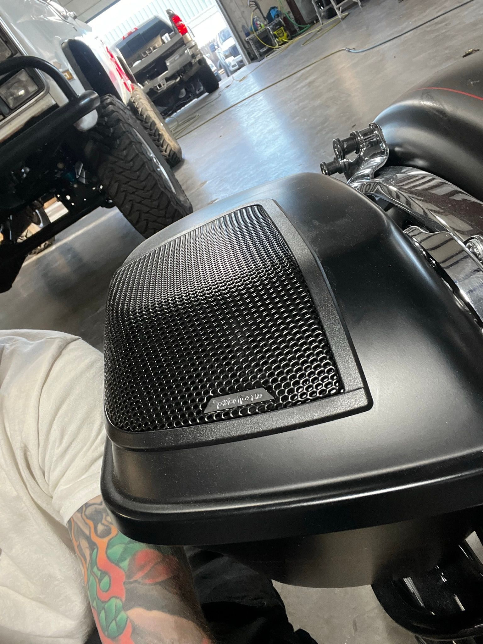 A man with tattoos is sitting next to a motorcycle in a garage.