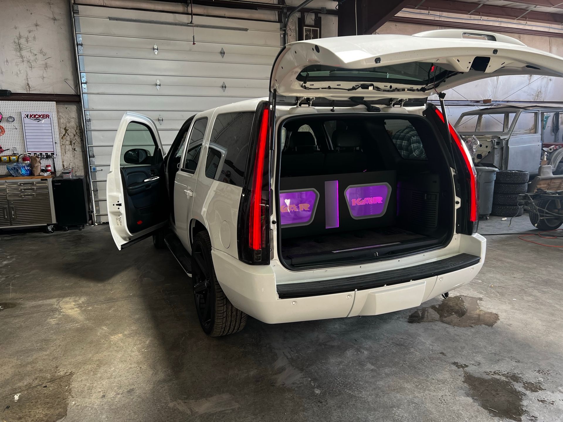 A white suv with purple speakers in the back is parked in a garage.