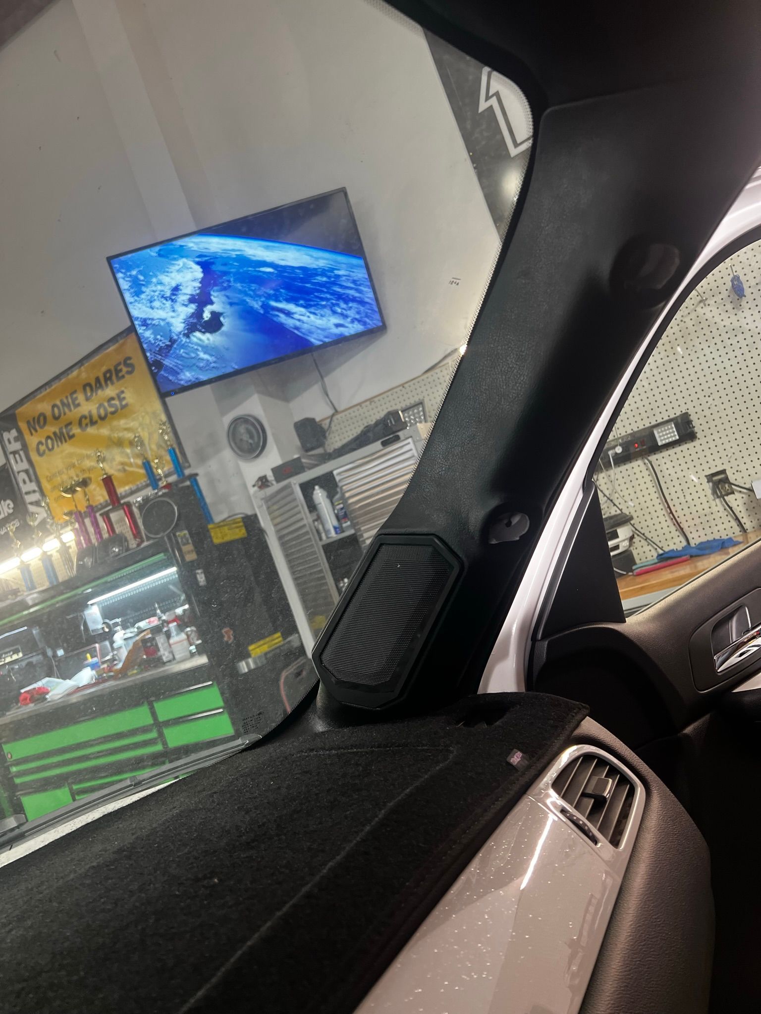 A car is parked in front of a store with a tv on the wall.