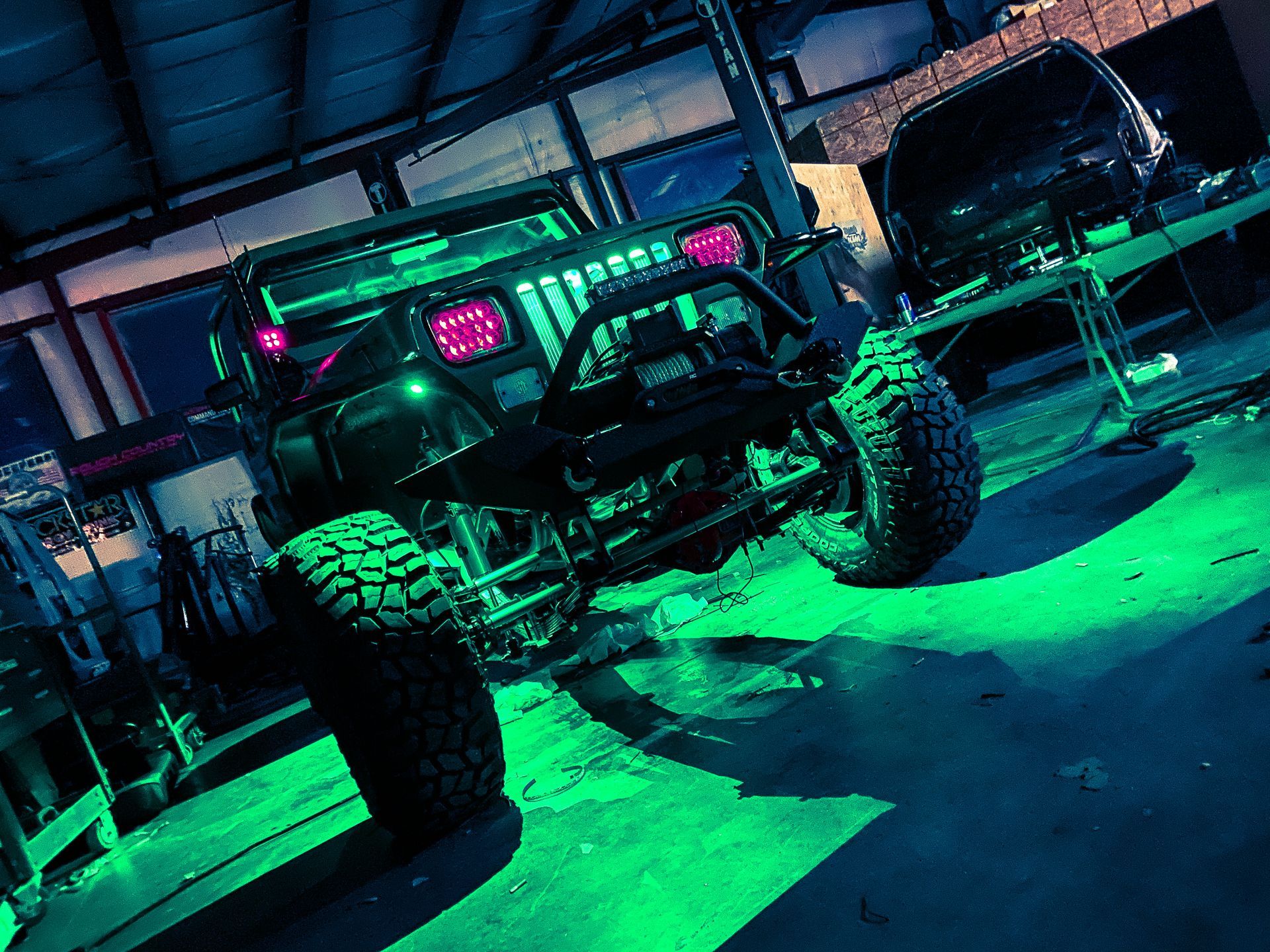 A jeep is parked in a garage under green lights