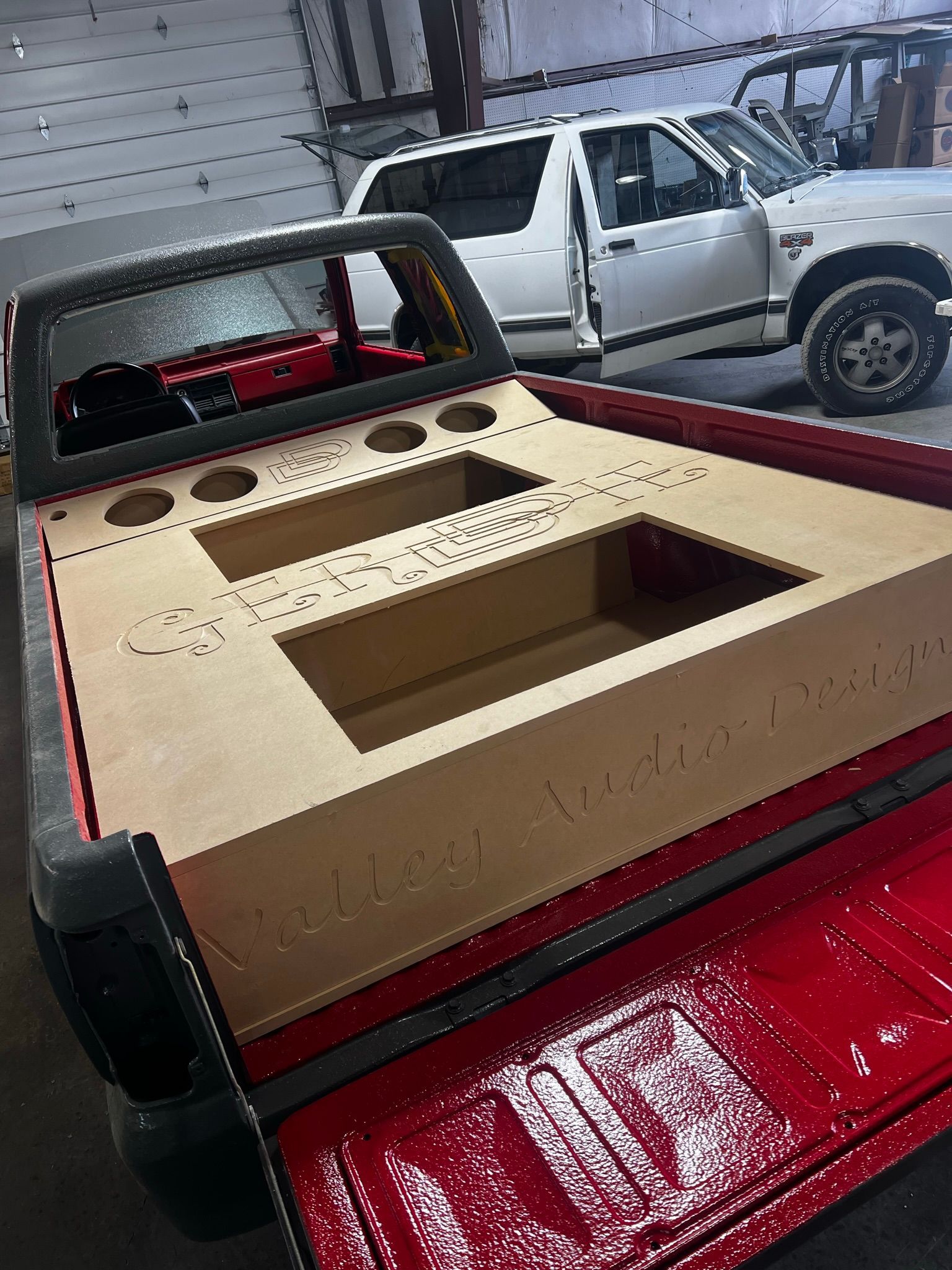 A red truck with a wooden box in the back is parked in a garage.