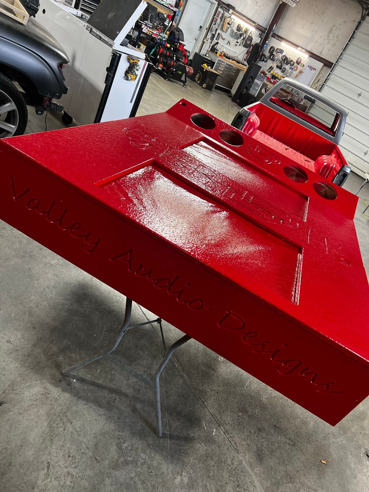 A red object is sitting on a table in a garage next to a red truck.