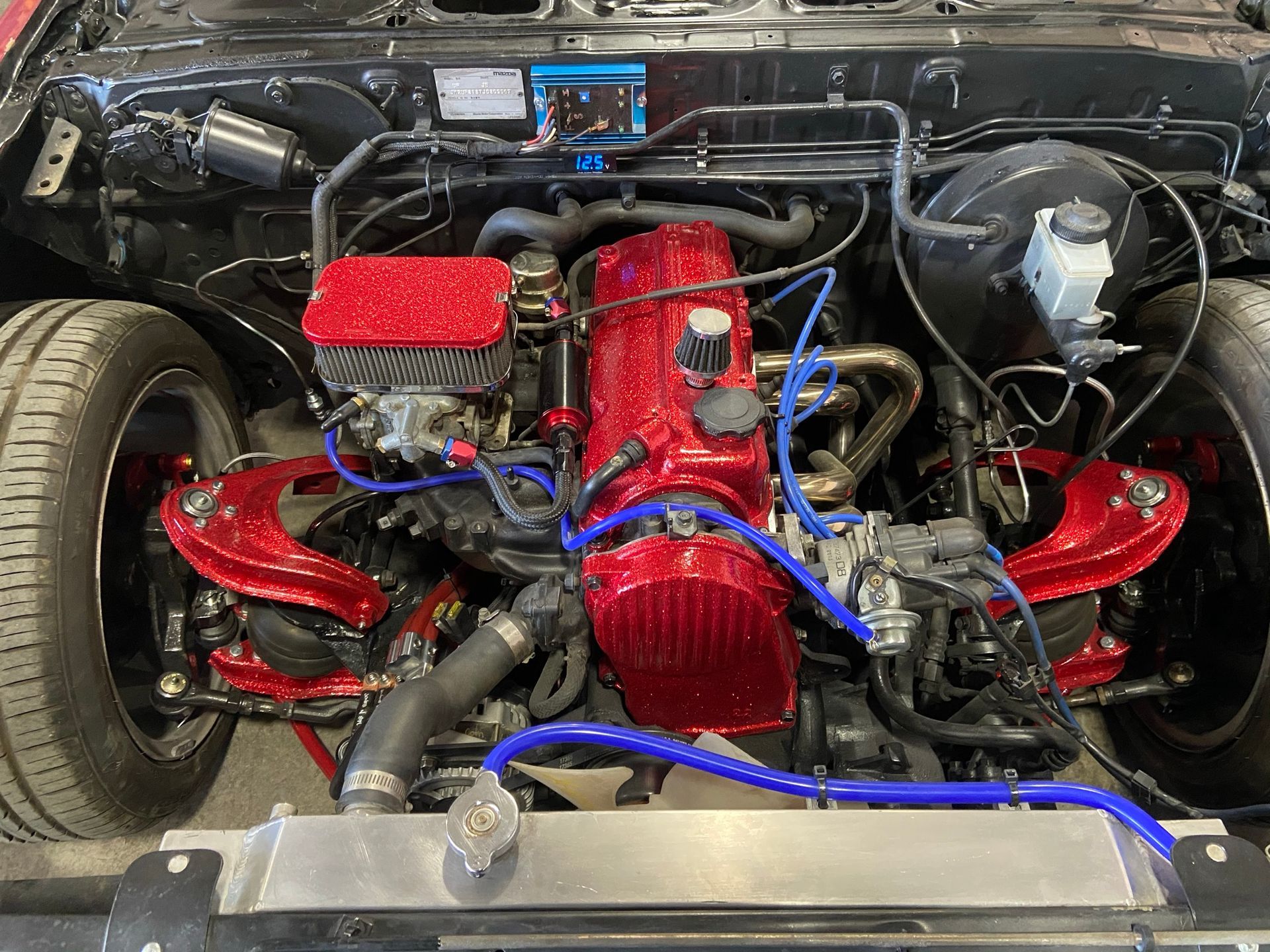 A red engine is sitting under the hood of a car.