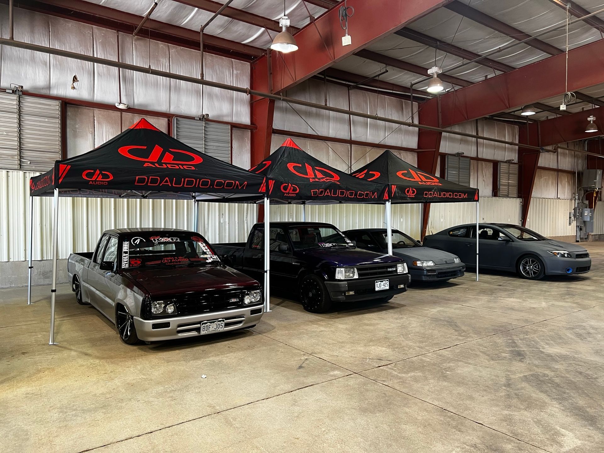 A row of cars are parked under tents in a garage.