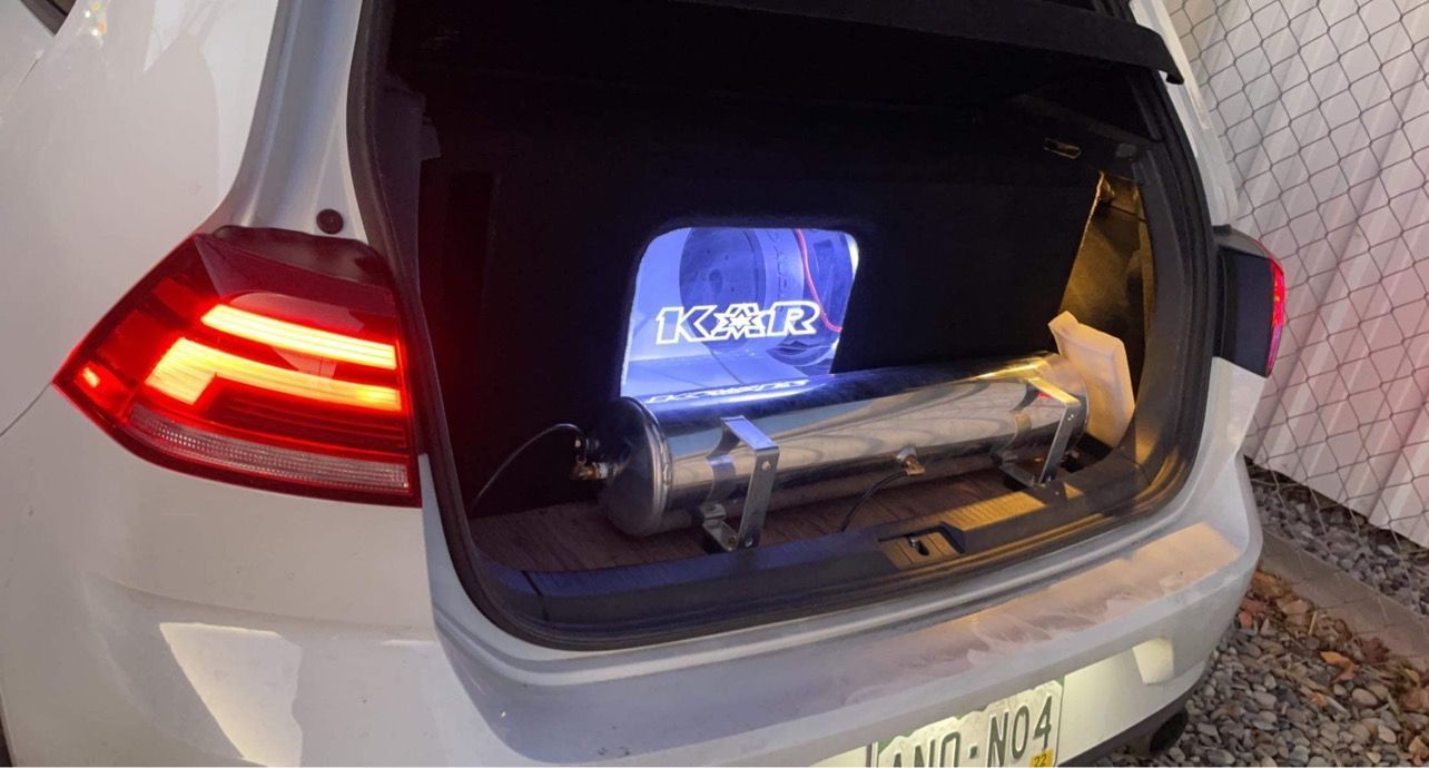 The trunk of a white car with a subwoofer in it.