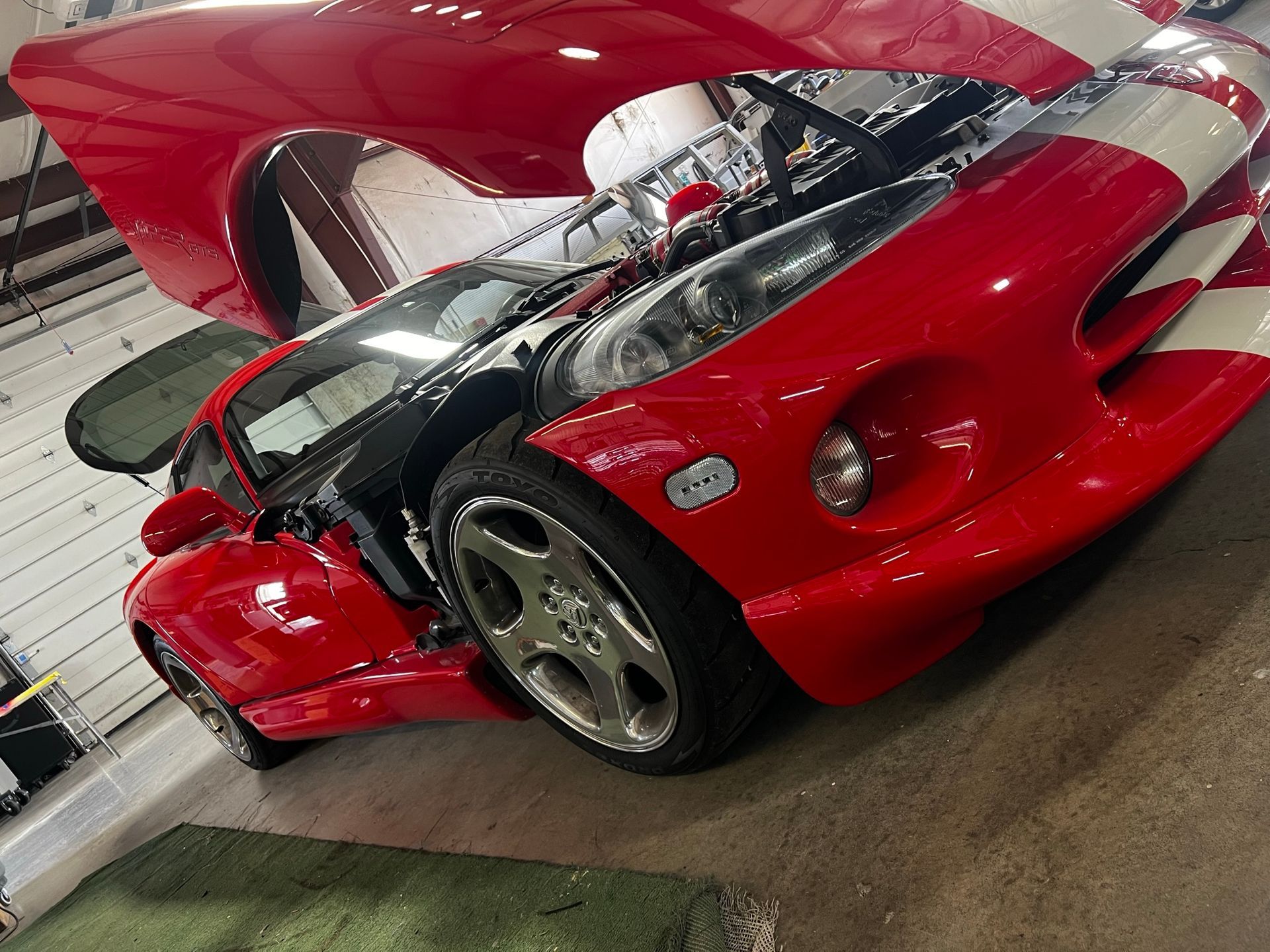 A red sports car with its hood up in a garage
