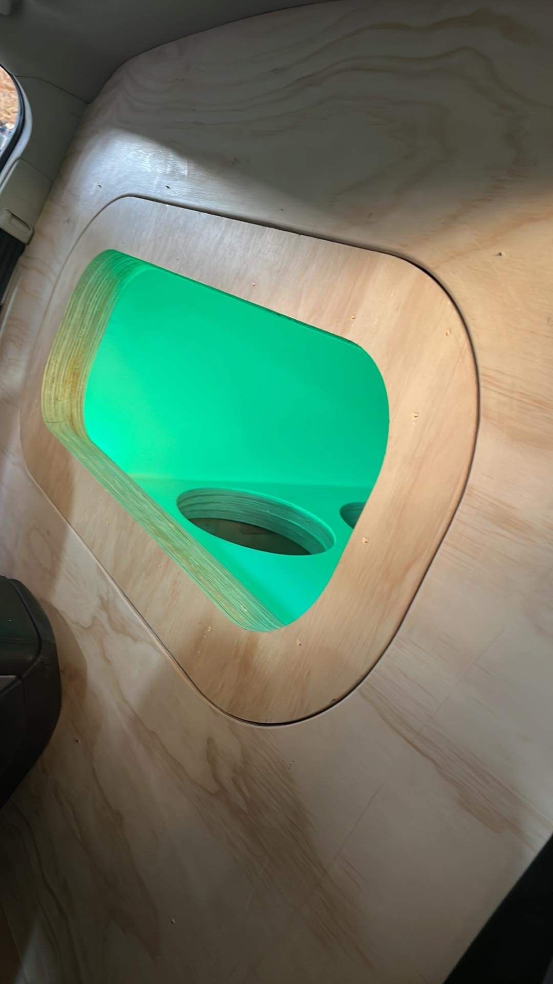 A hole in the floor of a car with a green light coming out of it.