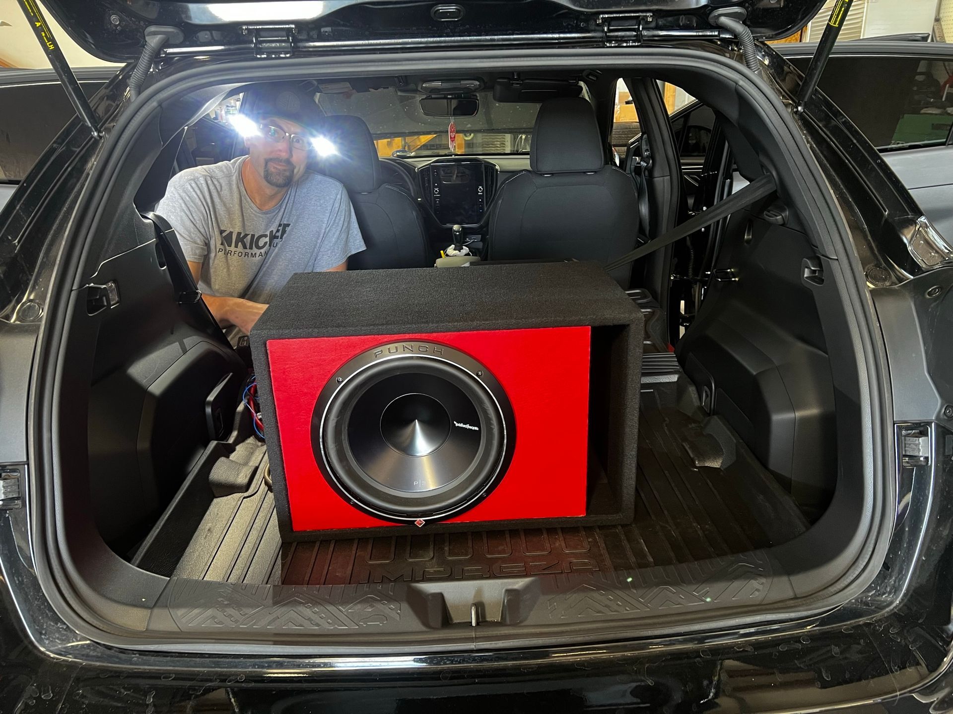 A man is sitting in the back of a car with a red subwoofer.