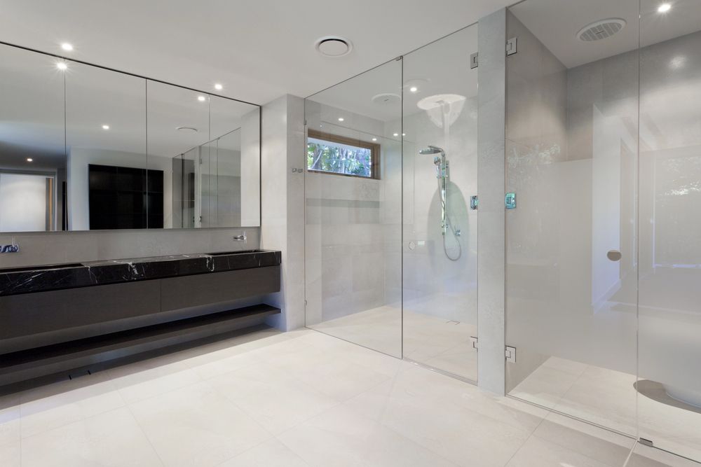 Baño moderno con cabina de ducha de cristal, paredes blancas y mueble de lavabo negro.