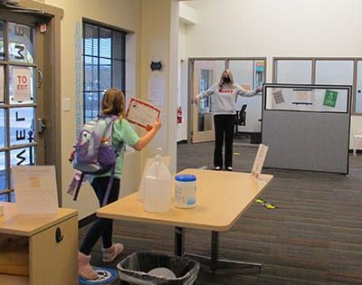 A girl with a backpack is standing next to a table in a room.