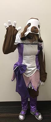 A person in a sloth mascot costume is standing in front of a wall.