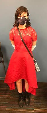 A woman wearing a red dress and a mask is standing in a room.