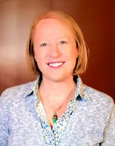 A woman in a blue jacket and green shirt is smiling for the camera.