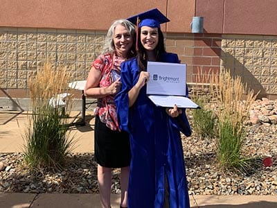 A woman is standing next to a woman in a graduation cap and gown holding a diploma.