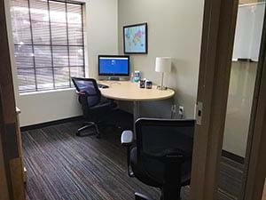 A small office with a desk and chairs and a computer.