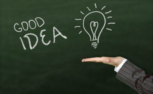 A person is holding a light bulb in front of a blackboard that says good idea