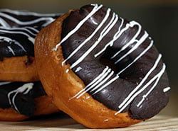 Three chocolate donuts with white frosting are stacked on top of each other on a wooden table.