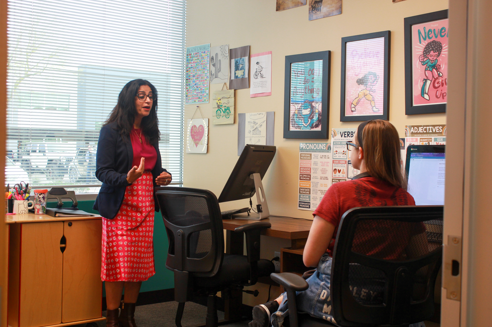 A woman is standing in an office talking to a woman sitting at a desk.