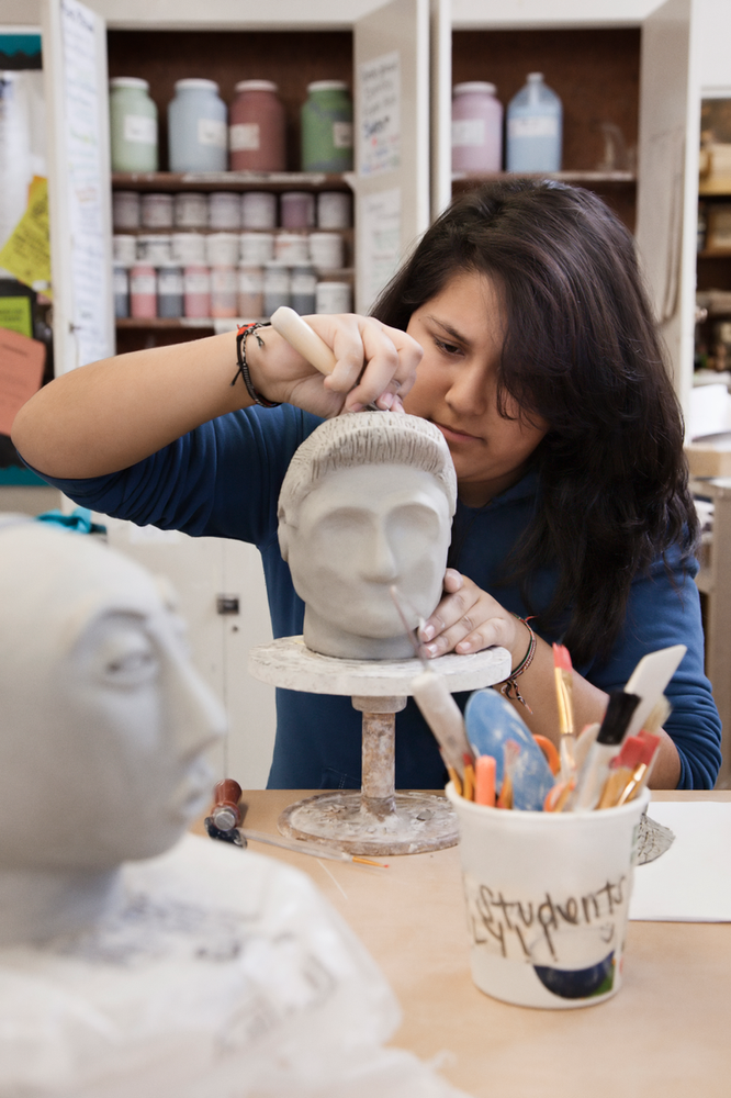 A woman is working on a statue of a man 's head in a studio.