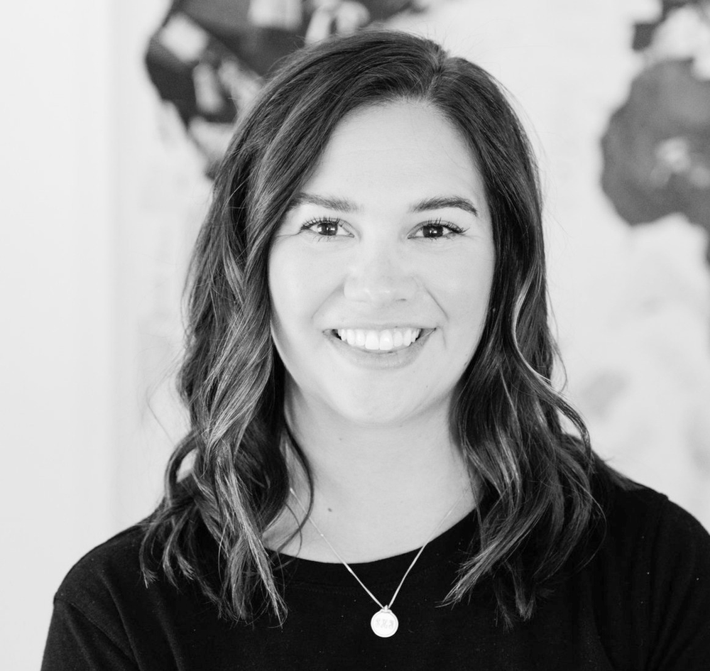 A woman wearing a black shirt and a necklace is smiling in a black and white photo.