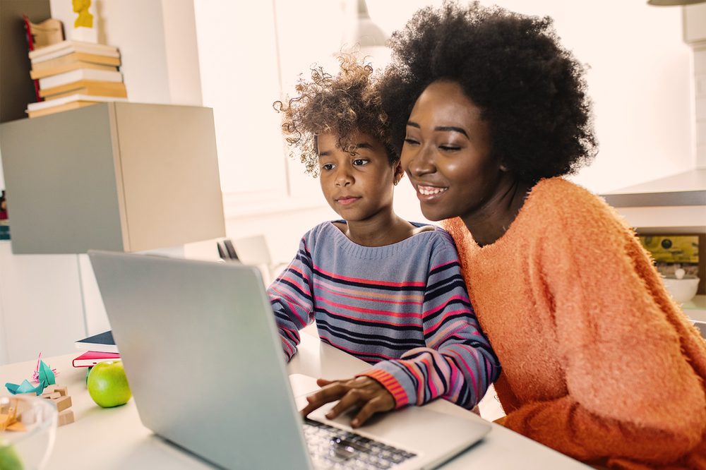 A woman and a child are sitting at a table using a laptop computer.