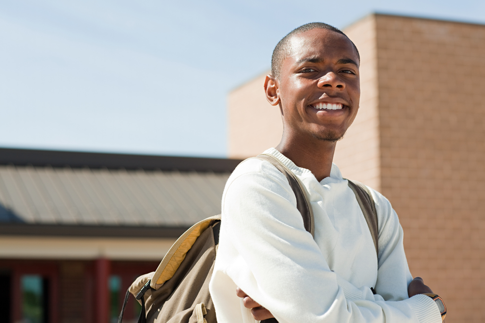 A young man with a backpack is standing in front of a building.