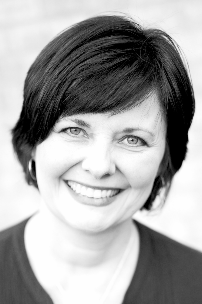 A woman with short hair is smiling in a black and white photo.