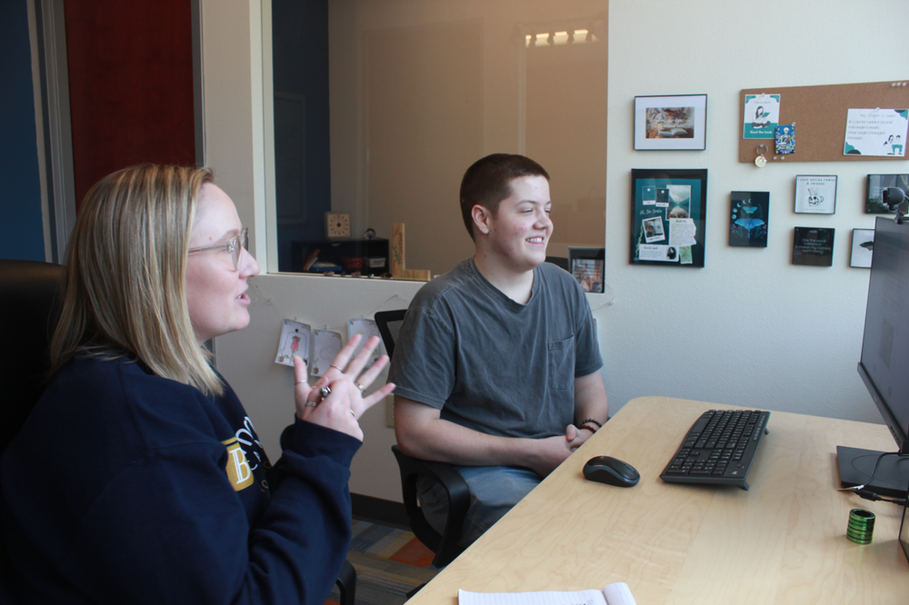 A man and a woman are sitting at a desk with a computer.