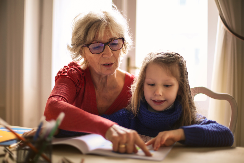 An elderly woman is helping a young girl with her homework.