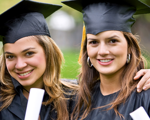 Two women wearing graduation caps and gowns are posing for a picture