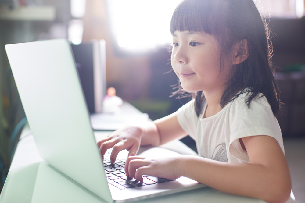 A little girl is typing on a laptop computer.