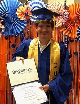 A young man in a graduation cap and gown is holding a diploma.