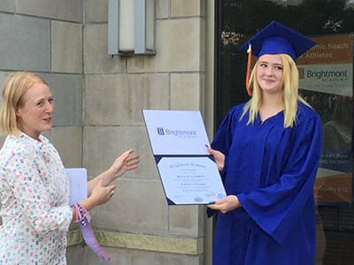 A woman in a graduation cap and gown is holding a certificate.