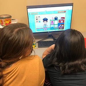 Two girls are sitting in front of a computer screen.