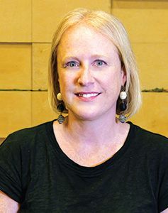 A woman in a blue jacket and green shirt is smiling for the camera.