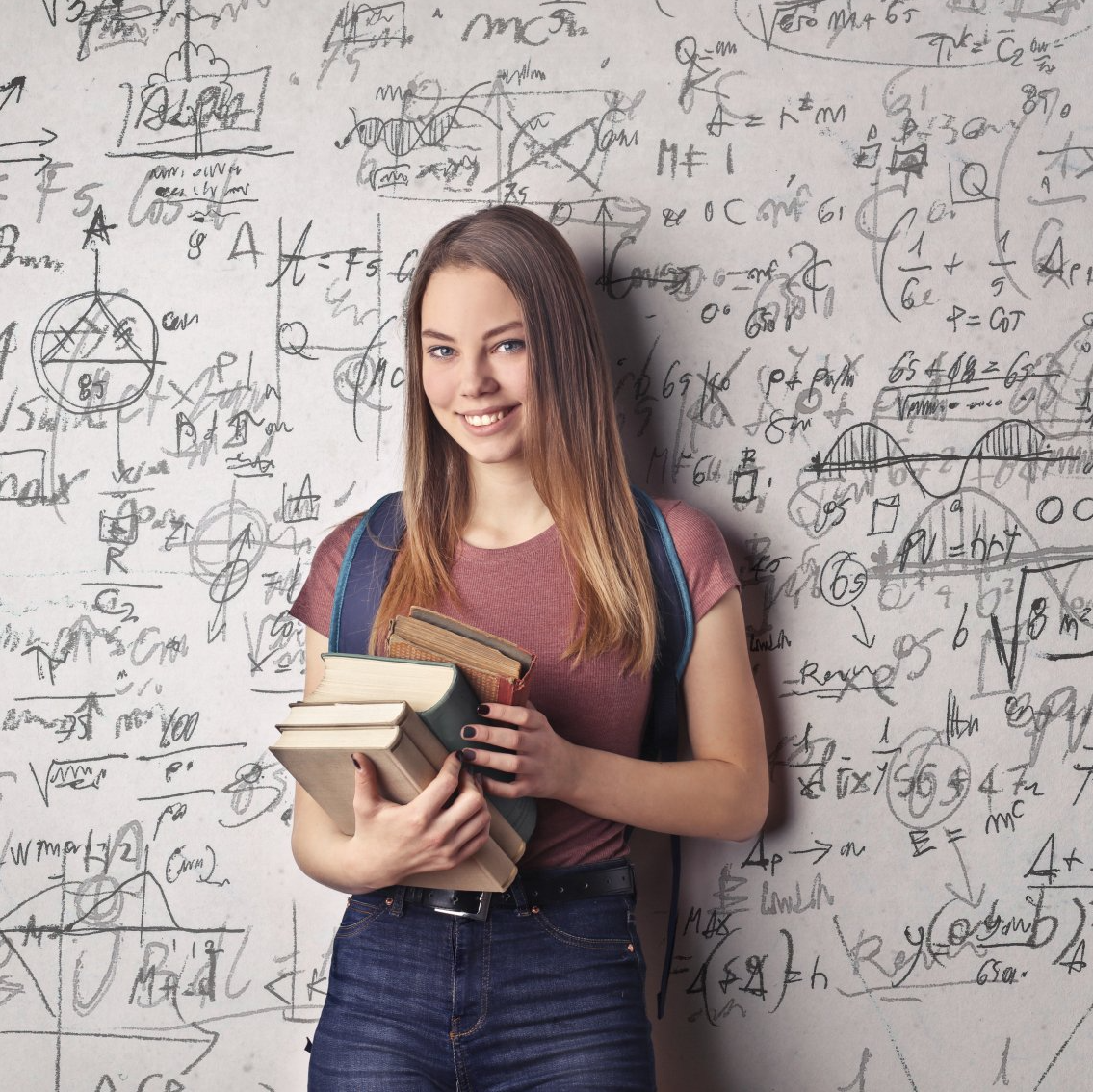 A woman is holding books in front of a wall with math equations on it